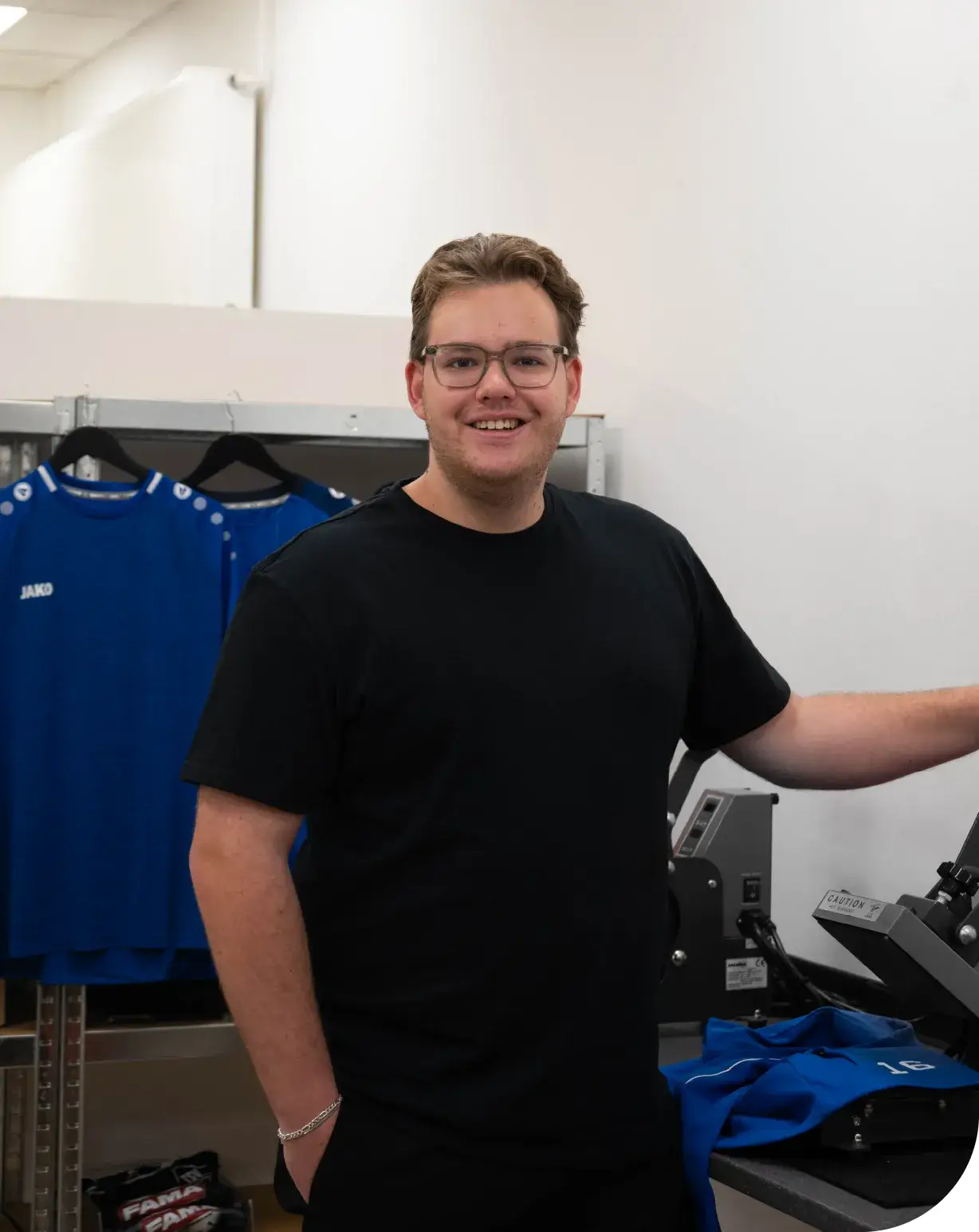 Noah Wilhelms, Inhaber von NW Werbetechnik Nordenham, in der Werkstatt bei der Textilveredelung mit Transferpresse und bedruckten Sporttextilien im Hintergrund